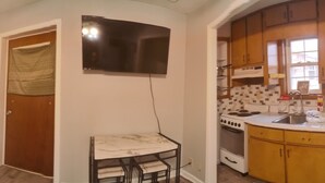Una habitación con cama, sofá, mesa de comedor y zona de cocina con armarios y electrodomésticos.