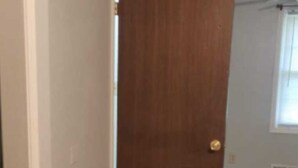 Una habitación con piso de madera, una puerta cerrada y una ventana con persianas.