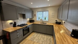 Een moderne keuken met grijze kastjes, een houten aanrechtblad, een ingebouwde magnetron en een raam met blinds.