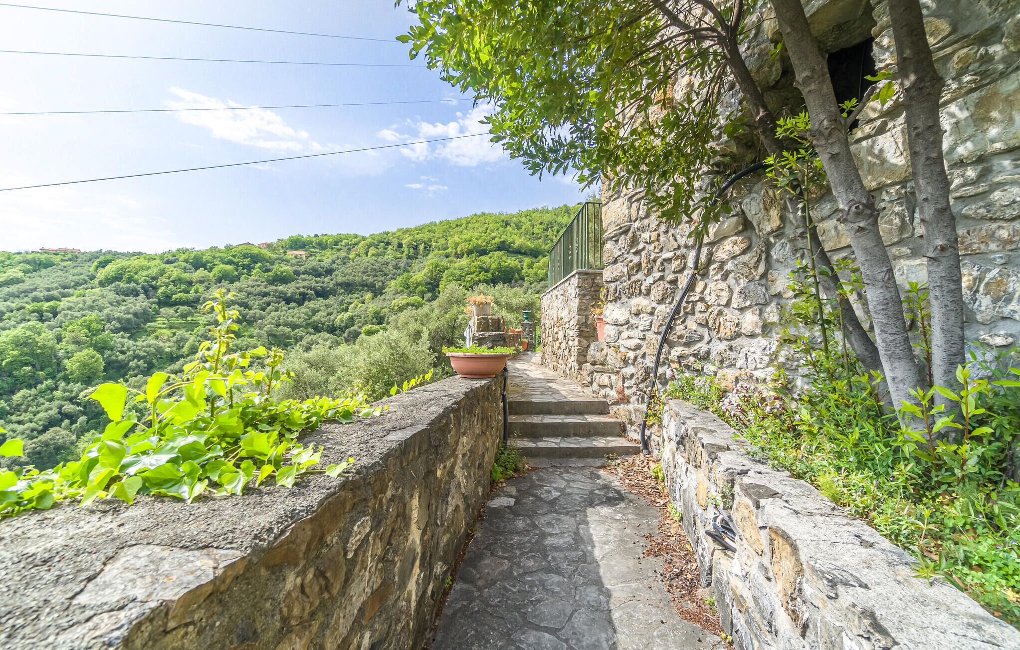 Eine Steintreppe führt zu einem Steinhaus mit Blick auf einen bewaldeten Hügel.
