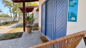 A covered outdoor area with a blue door, a wicker chair, and a potted plant. - Vila Carijós (Florianópolis)