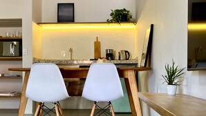 A modern kitchen with a central island, two white chairs, and a wooden table. - Vila Carijós (Florianópolis)