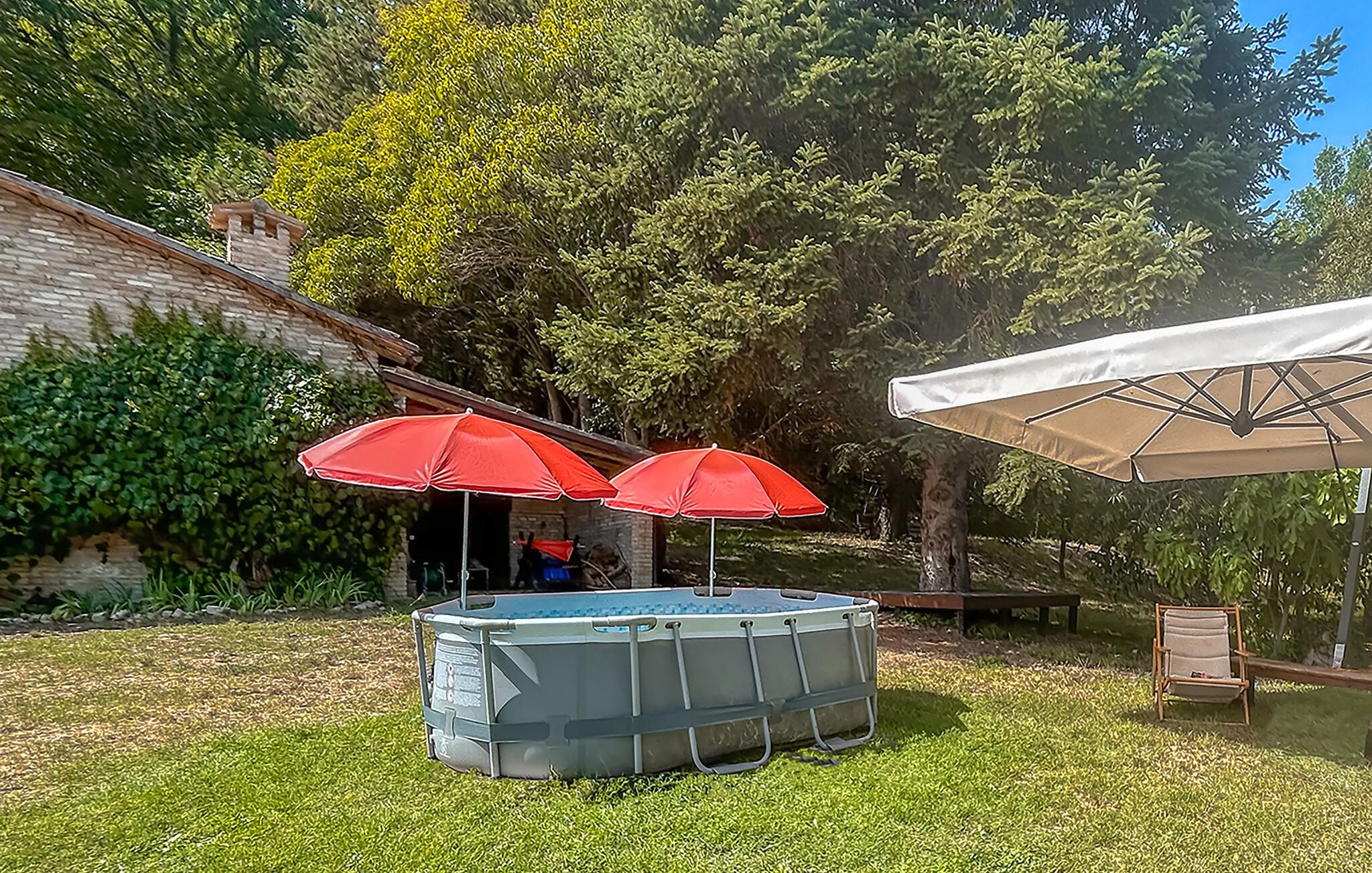 A backyard with a swimming pool, two red umbrellas, a beige umbrella, and a wooden bench.