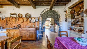 Une cuisine rustique avec des meubles en bois, une table à manger et des chaises. Un grand arc donne accès à une autre pièce.