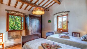 Une chambre avec deux lits, des poutres apparentes, une grande fenêtre et une lampe suspendue.