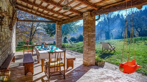 Un espace extérieur rustique aménagé avec des sièges, une table dressée pour le repas, entouré de meubles en bois et agrémenté d’une balançoire suspendue.