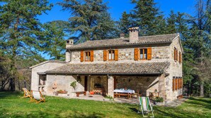 Une maison en pierre avec un toit en tuiles, des volets en bois et un porche doté de sièges pour l’extérieur.