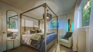A four-poster bed with a canopy, a bedside table with a lamp, a chair, and a large mirror.