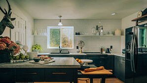 A modern kitchen with a marble island, a refrigerator, and a window with a view of trees.