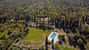 An aerial view of a property with a swimming pool, surrounded by dense forest and a hilly landscape.