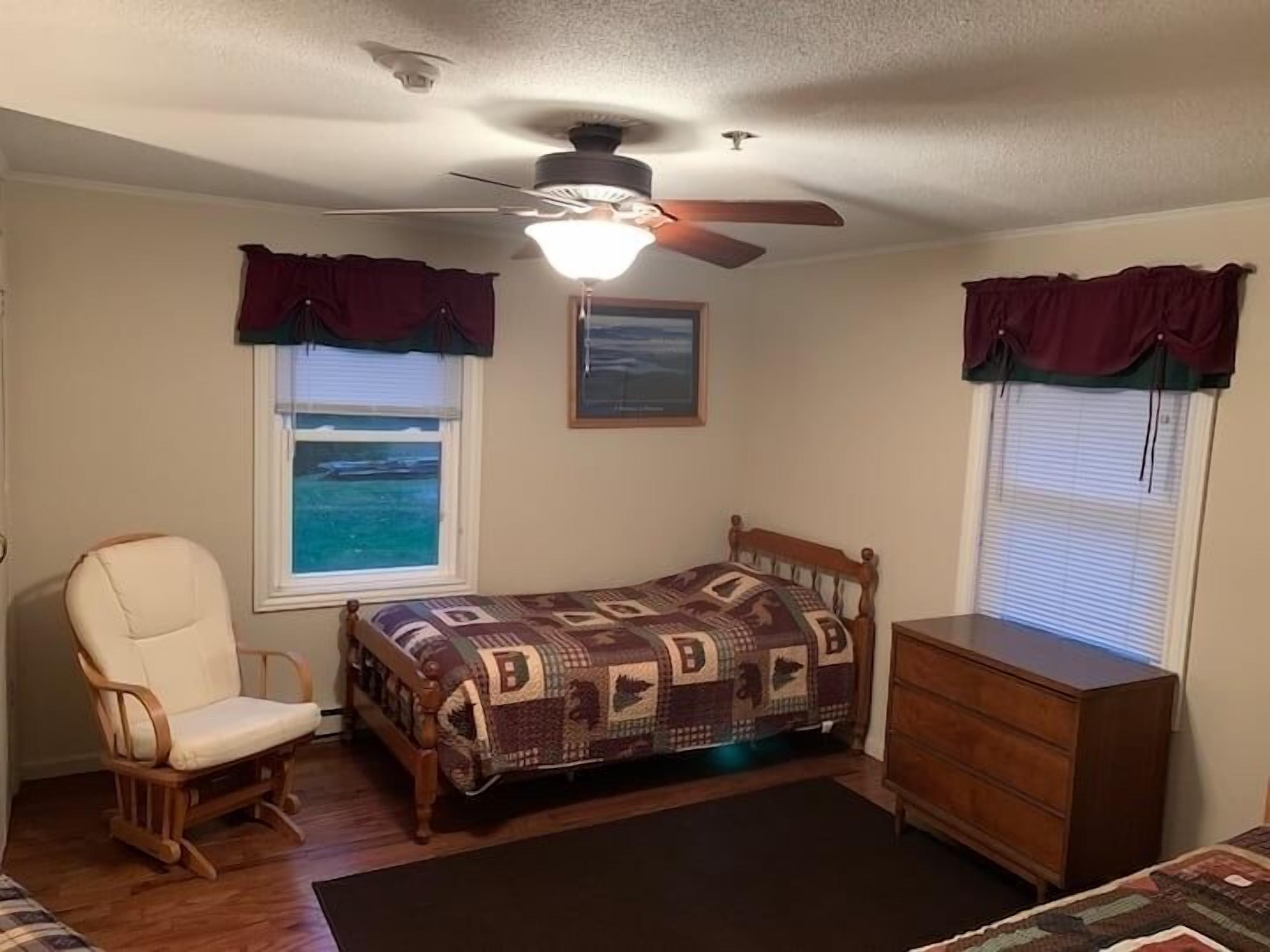 Une chambre à coucher comprenant un lit, une chaise, une commode et un ventilateur de plafond.