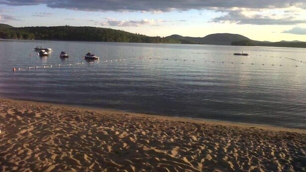 Una playa con barcos en el agua y una colina boscosa al fondo.