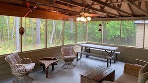Un interior rústico de madera con un ventanal grande que da a un bosque, una mesa de madera y dos sillas.