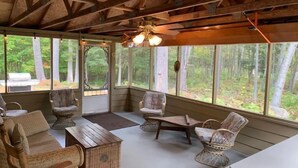 Un espacio de estar al aire libre techado con muebles de madera y ventanas amplias que ofrecen vistas al bosque.