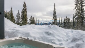 Un bain à remous entouré d’un paysage enneigé et d’arbres à feuilles persistantes.