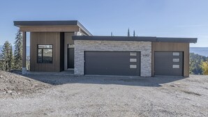 Une maison moderne à deux étages, dotée d’un garage, d’une façade en pierre et de grandes fenêtres.