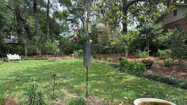 Un jardín con comedero para pájaros, un banco y una fuente de agua.