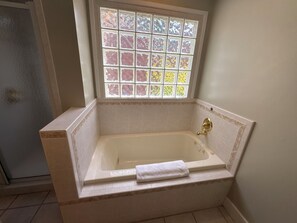 Un baño con una bañera independiente, un ventanal con diseño calado y una toalla en la bañera.