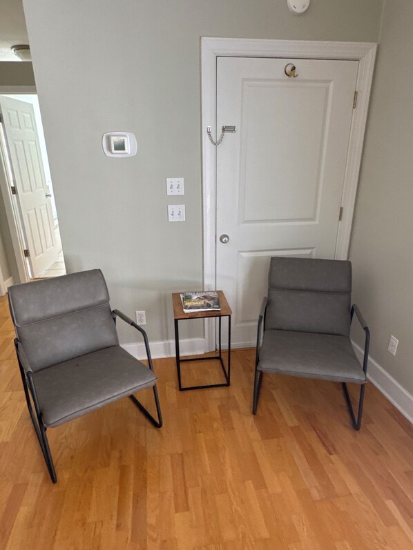 Two grey chairs, a small wooden table with a magazine, and a white door with a keyhole. - Villas @ Lake Ella Flat: 1br-1bth-desk (Tallahassee)