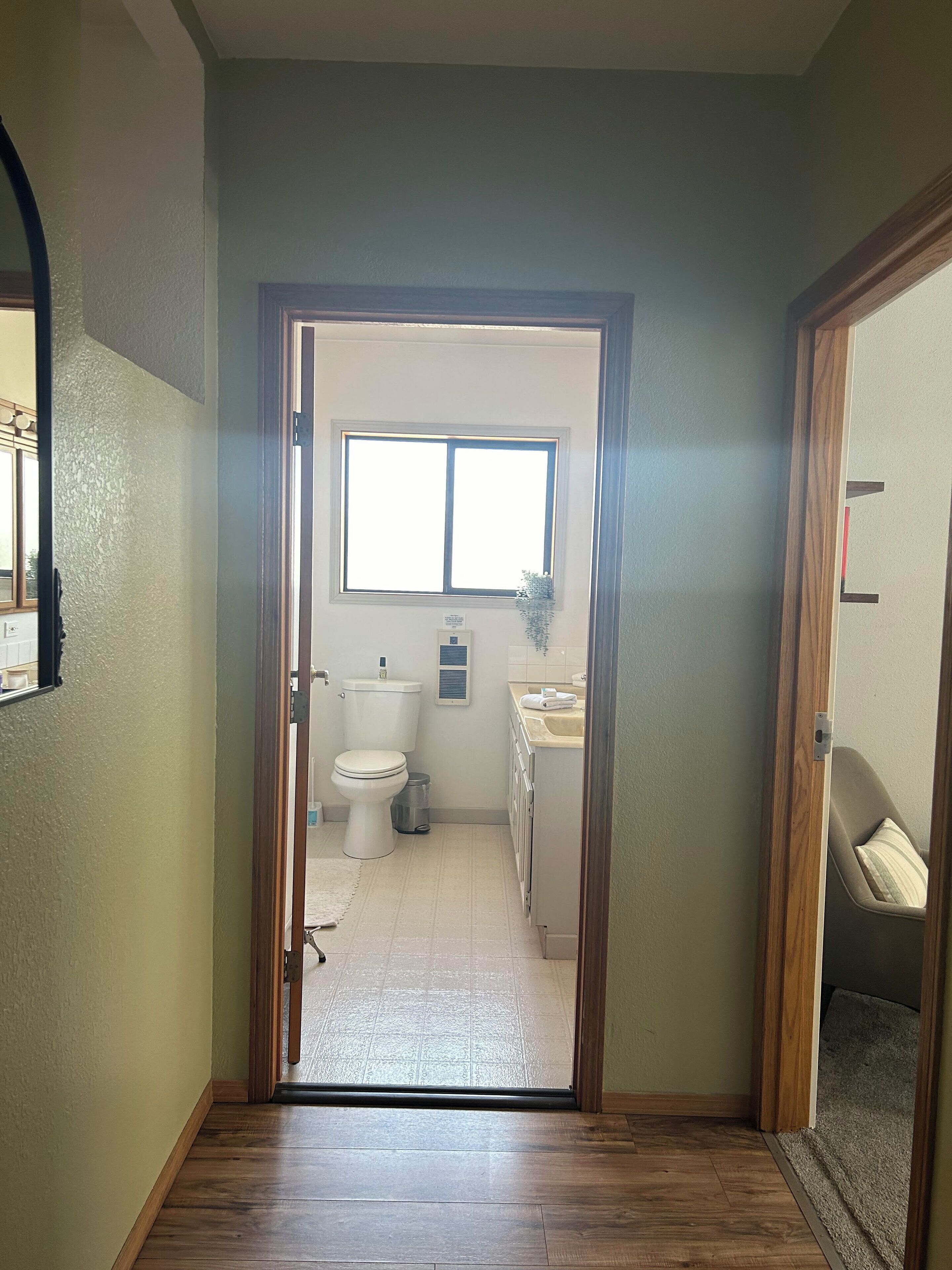 Pasillo que conduce a un baño con inodoro, lavamanos y ventana.