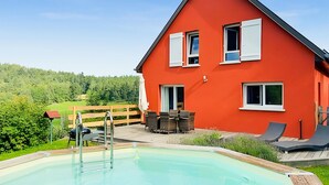 Una casa roja con piscina, mobiliario exterior y terraza de madera.