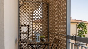 Un balcón con una mesa y sillas de madera, baranda metálica y celosía.