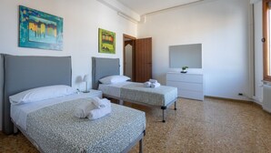 Habitación de hotel con dos camas, una mesita de noche, cómoda, espejo y obras de arte en las paredes.