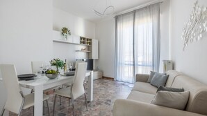 Una sala moderna con comedor, un sofá y una cocina con estantes y una planta.