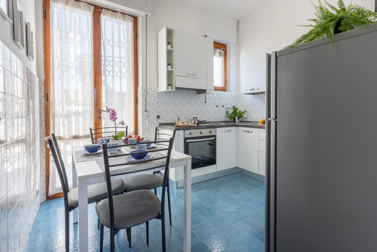 Una cucina con mobili bianchi, un tavolo da pranzo con sedie, un frigorifero e una finestra con tende.