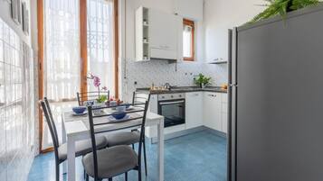 Una cucina con mobili bianchi, un tavolo da pranzo con sedie, un frigorifero e una finestra con tende.