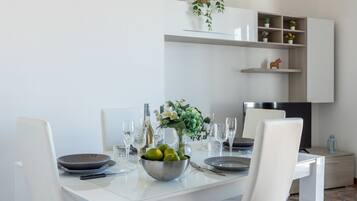 Un'elegante sala da pranzo moderna con un tavolo bianco apparecchiato per quattro persone, una ciotola di frutta e un vaso di fiori.