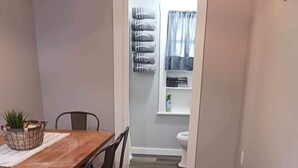 A dining area with a wooden table and chairs, a trash bin, and a potted plant.
