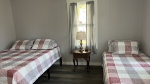 A bedroom with two beds, a nightstand with a lamp, and a window with curtains.