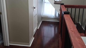 A staircase with a wooden handrail leading to a landing, a door on the left, and a window at the top of the stairs.