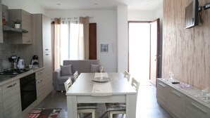 A modern kitchen with a dining area, a sofa, and a TV mounted on the wall. - Al Civico 5 - Bright Apartment W/ Private Parking! (Decimomannu)