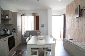 A modern kitchen with a dining area, a sofa, and a TV mounted on the wall.