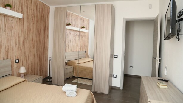 A modern bedroom with a bed, bedside table, lamp, and a TV mounted on the wall. - Al Civico 5 - Bright Apartment W/ Private Parking! (Decimomannu)