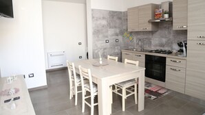 A modern kitchen with a dining table, chairs, a TV, and a built-in oven. - Al Civico 5 - Bright Apartment W/ Private Parking! (Decimomannu)