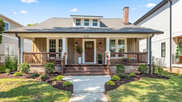 A two-story house with a front porch, a brick chimney, and a number "1118" on the front door. - Large 4BR Home Near Broadway with Hot Tub and Private Backyard (Nashville)