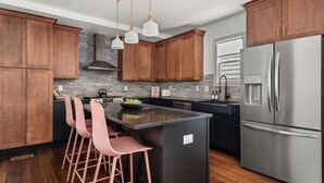 A modern kitchen with wooden cabinets, a stainless steel refrigerator, and a central island with bar stools. - Large 4BR Home Near Broadway with Hot Tub and Private Backyard (Nashville)
