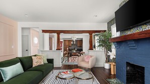 A living room with a green sofa, a pink armchair, a fireplace, and a dining area in the background. - Large 4BR Home Near Broadway with Hot Tub and Private Backyard (Nashville)
