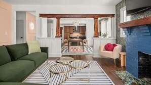 A living room with a green sofa, a white armchair, and a blue fireplace. - Large 4BR Home Near Broadway with Hot Tub and Private Backyard (Nashville)