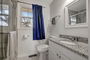 A bathroom with a white toilet, a sink with a granite countertop, and a shower with a glass door.