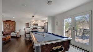 A pool table in a spacious room with a dining area, a wooden cabinet, and a view of a deck through a glass door.