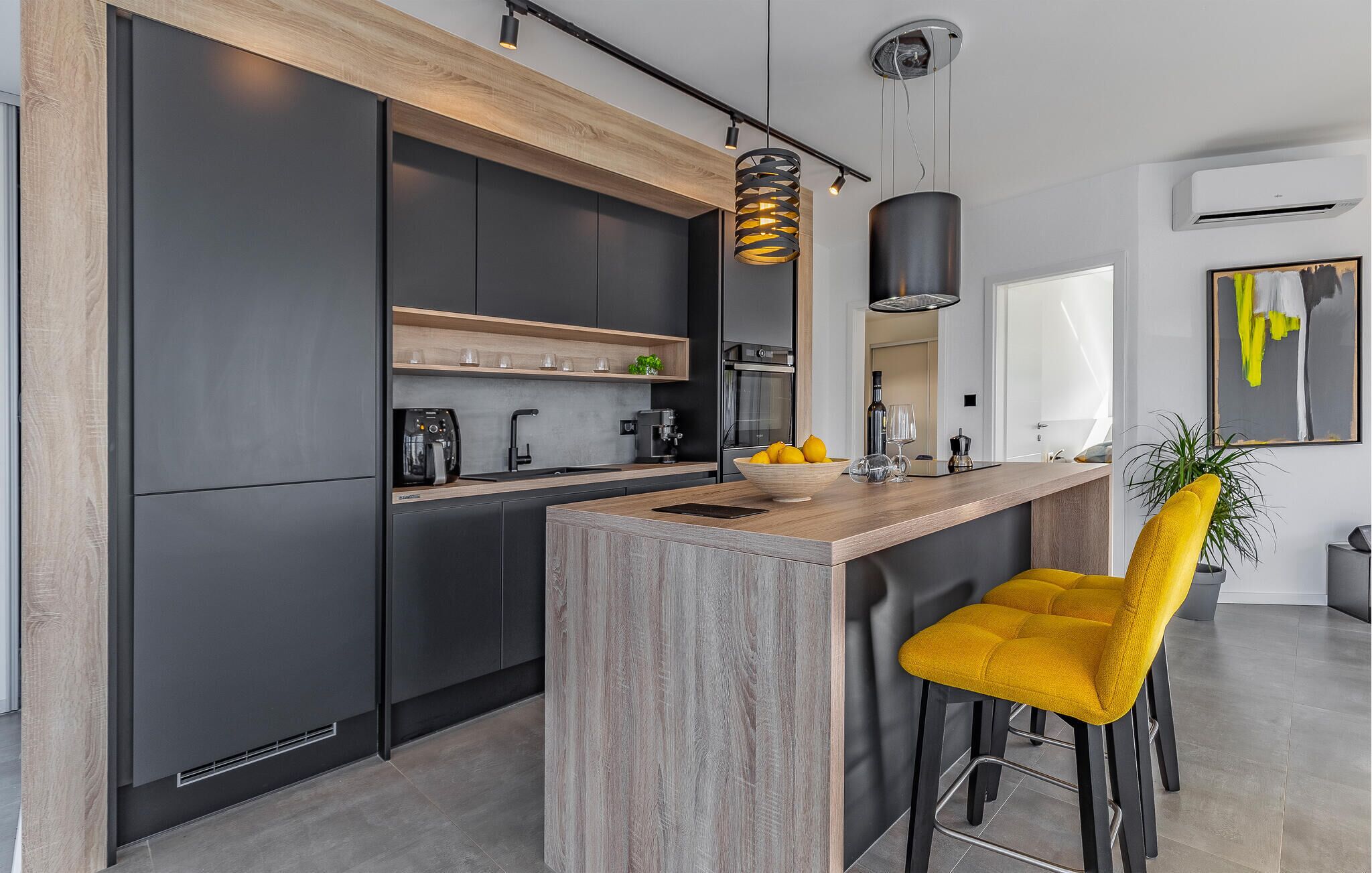 A modern kitchen with dark cabinetry, a wooden countertop, and a bar area with a yellow chair.