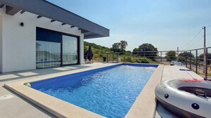 Ett modernt hus med en rektangulär swimmingpool och ett bubbelbad.