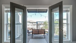 Une pièce dotée d’une grande porte-fenêtre coulissante donnant sur un balcon équipé d’un banc et de guirlandes lumineuses.