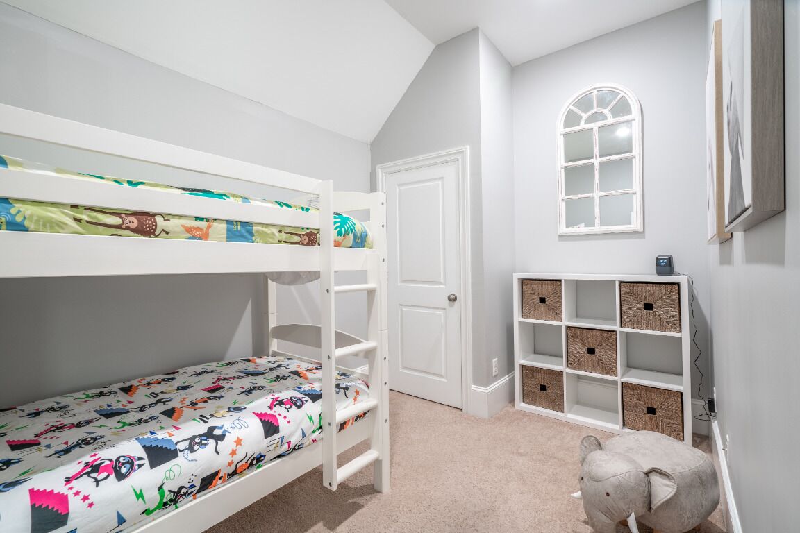 Un lit superposé pour enfant avec une couverture colorée, une porte blanche, un petit jouet en forme d’éléphant et une étagère blanche avec des paniers.