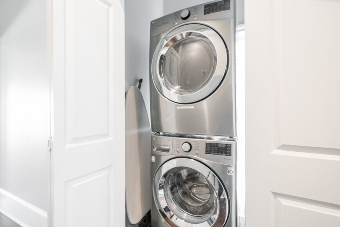 Uma máquina de lavar e secar empilhadas em um quarto com paredes brancas.