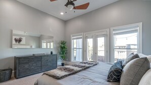 Une chambre à coucher avec un lit, une commode, un miroir, une plante en pot et de grandes fenêtres.
